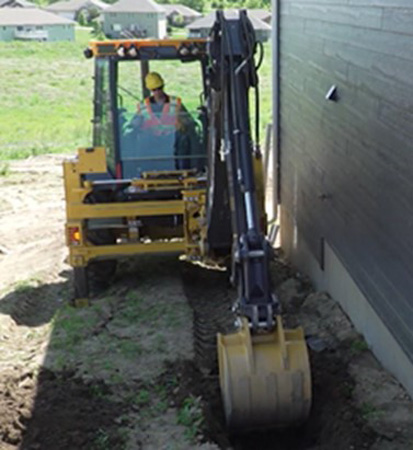 315SL sideshift backhoe trenching next to a wall